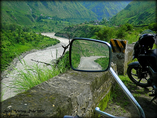 looking over a river flowing through a lush green valley, seen from a motorcycle